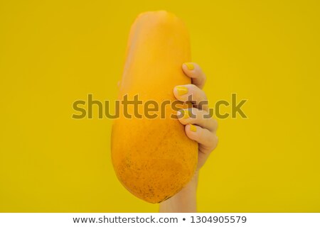 ストックフォト: Hand With A Yellow Manicure Holding A Orange Ripe Papaya On A Yellow Background