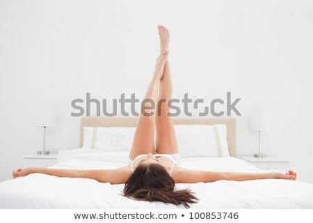 Foto d'archivio: Smiling Young Woman Lying On The Bed With Raised Legs Up