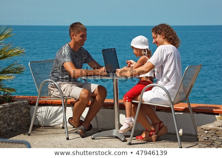 Foto d'archivio: Family Of Three People Resting On Sea Daughter Sits On His Lap Mother They Use Laptop