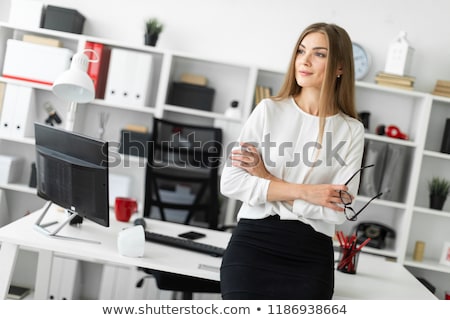 Foto d'archivio: A Young Girl Is Standing Leaning On A Table In The Office And Holding Glasses In Her Hand