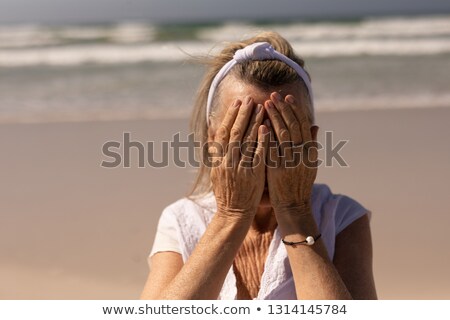 Foto d'archivio: Front View Of Worried Senior Woman Covering Her Face While Standing On The Beach