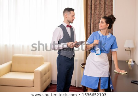 Сток-фото: Pretty Room Maid Cleaning Table While Looking At Porter During Conversation