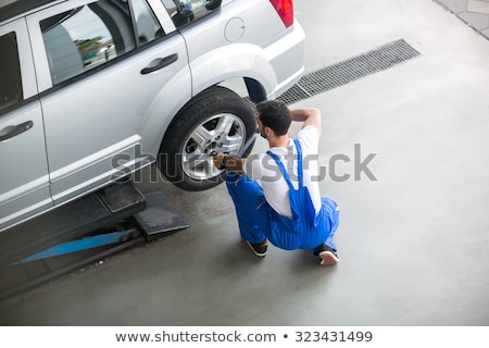 Stock photo: Male Mechanic Using Pneumatic Wrench To Fix Car Tire