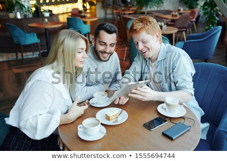 Сток-фото: Cheerful Guy With Touchpad Showing His Friends Curious Stuff By Table In Cafe
