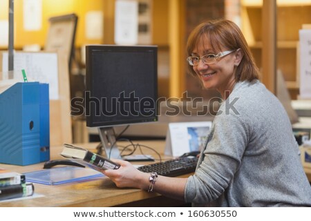 Stok fotoğraf: Smiling Female Librarian Holding A Book Standing Behind The Desk