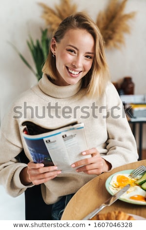 Stok fotoğraf: Photo Of Joyful Blonde Woman Reading Magazine While Having Breakfast