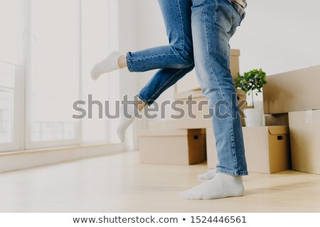 [[stock_photo]]: Happy Unknown Couple Move In New Abode Man Lifts Woman Wear Jeans Pose In Empty Room With Carton