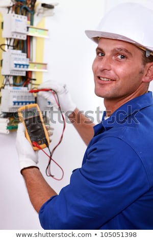 Stockfoto: Smiling Electrician Using Multimeter On Electric Meter