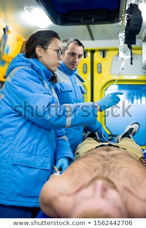 Foto stock: Two Young Paramedics Preparing Dropper For Sick Man Inside Ambulance Car