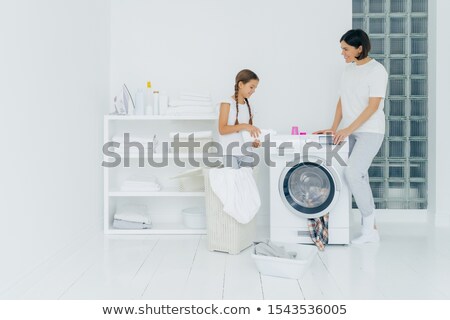 Stok fotoğraf: Indoor Shot Of Happy Mother And Daughter Stand Near Washing Machine Girl Pours Liquid Powder Load