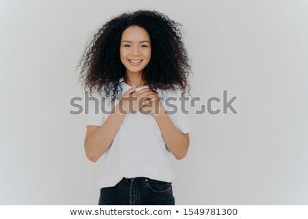 Stockfoto: Photo Of Cheerful Woman With Afro Hair Keeps Hands On Chest Expresses Gratitude Smiles Gently We
