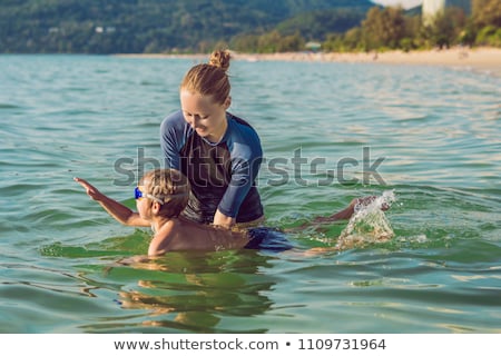 Stockfoto: Woman Swimming Instructor For Children Is Teaching A Happy Boy To Swim In The Sea