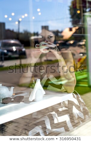 Foto stock: Enina · sentada · em · um · sofá · e · usando · o · telefone · atrás · da · janela · de · vidro