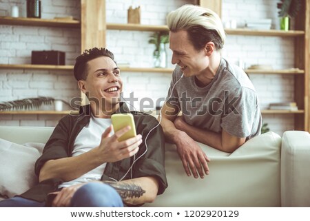 Zdjęcia stock: Cheerful Man With Dark Hair Smiling While Holding Smartphone And