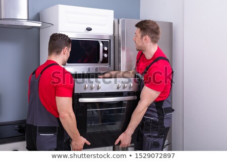 Foto d'archivio: Young Male Worker Placing Modern Oven In Kitchen