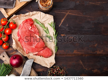 ストックフォト: Fresh Raw Organic Slice Of Braising Steak Fillet On Butchers Paper With Fork And Knife On Dark Woode