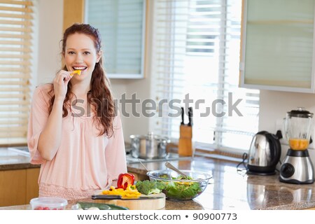 Foto d'archivio: Young Woman In Kitchen Nibbling On A Cucumber