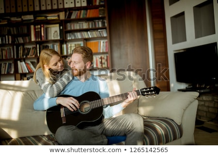 Foto d'archivio: Man Playing Acoustic Guitar On The Sofa For His Young Beautiful