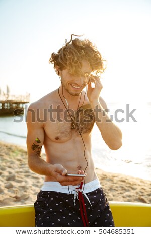 ストックフォト: Handsome Curly Surfer Listening Music With Smartphone At The Beach