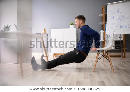 Stock photo: Businessman Doing Triceps Dips In Office