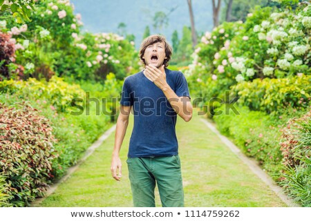 Foto stock: Young Man Sneeze In The Park Against The Background Of A Flowering Tree Allergy To Pollen Concept