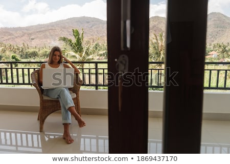 ストックフォト: Young Woman Is Working On A Laptop On Her Balcony Overlooking The Skyscrapers Freelancer Remote Wo