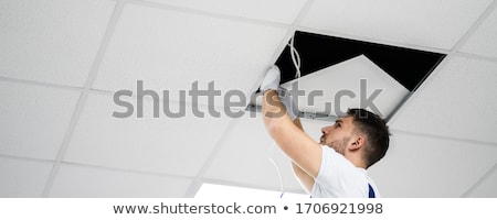 Stock photo: Electrician On Stepladder Installs Lighting To The Ceiling