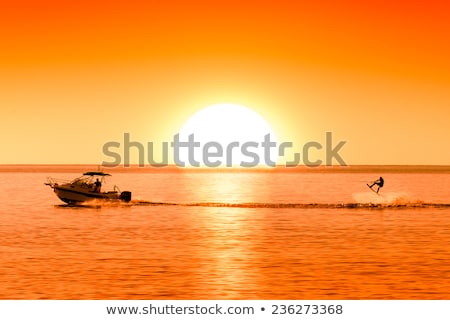 Stock fotó: Silhouette Of Motor Boat And Wakeboarder At Sunset Performing Crazy Trick