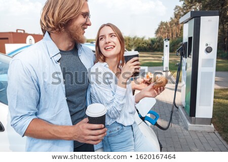 [[stock_photo]]: Young Woman Laughing By Electric Car