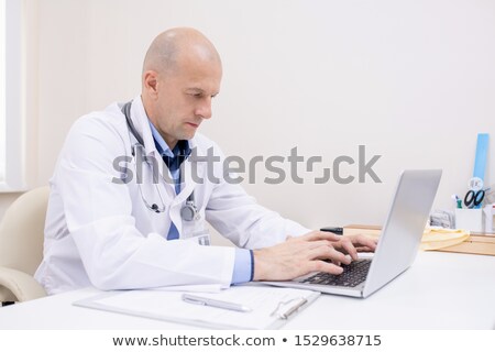 Stock photo: Bald Male Professional In Whitecoat Concentrating On Work In Front Of Laptop