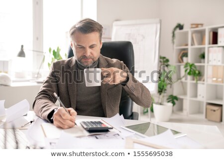 Сток-фото: Serious Mature Accountant With Pen And Cup Of Coffee Making Calculations