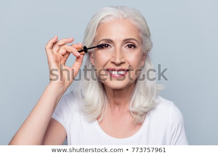 Stok fotoğraf: Smiling Senior Woman Applying Mascara To Eyelashes