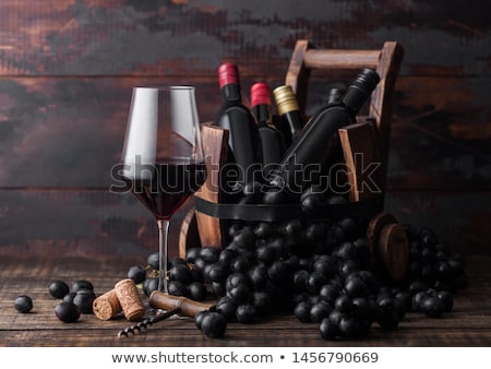 Stok fotoğraf: Elegant Glass Of Red Wine With Dark Grapes And Mini Bottles Of Wine Inside Vintage Wooden Barrel On