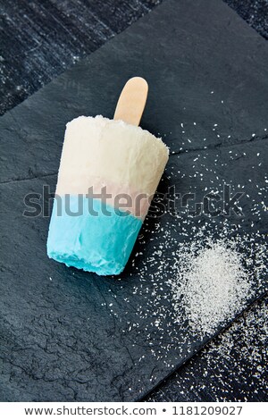 Multicolored Ice Cream On A Stick With Coconut Crumb Represented On A Black Slate On A Dark Concrete Stockfoto © artjazz