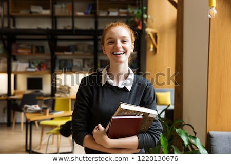 Foto stock: Redhead Lady Student Posing Indoors In Library Holding Books Listening Music With Earphones Using Mo