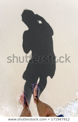 Foto stock: Man Is Throwing Shadow To The Fine Sand Of The Beach Showing The Complete Body In A Smoth Circle