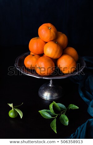 Stockfoto: Tangerines Stacked On Metal Dish Small Immature Mandarin And Branch With Leaves