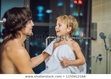 Imagine de stoc: Dad Wipes His Son With A Towel After A Shower In The Evening Before Going To Sleep On The Background