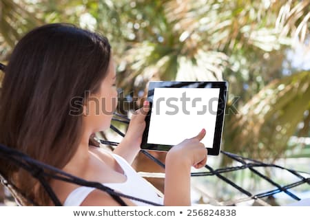 Stok fotoğraf: Woman In Sitting On Hammock Using Digital Tablet At Beach