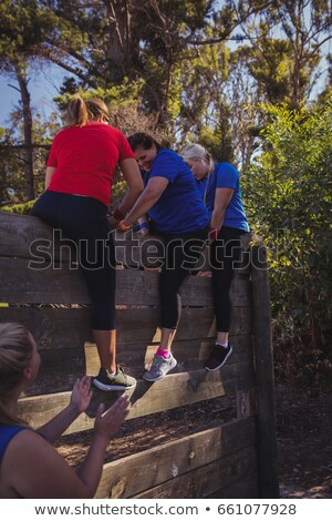 Сток-фото: Woman Being Assisted By Her Teammates To Climb A Wooden Wall During Obstacle Course Training