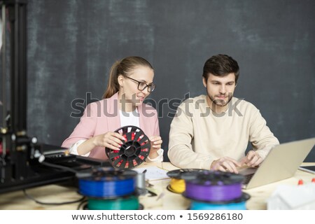 Foto stock: Young Creative Colleagues With Spools Of Filaments Sitting In Front Of Laptop
