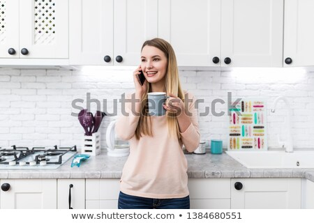 Foto stock: Woman Drinking Coffee And Talking On Mobile Phone At Kitchen