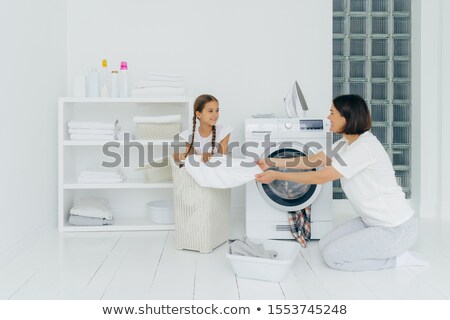 Foto stock: Little Kid Helps Mum With Washing Sits In Basket With Laundry Busy Housewife Does Housework Washe