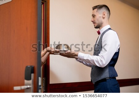 Zdjęcia stock: Young Hospitable Waiter In Uniform Passing Cloche With Lunch To Female Guest