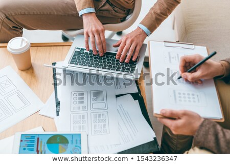 Foto stock: Software Developer Typing While His Colleague Making Sketches Of Interface