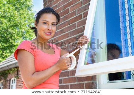 Stockfoto: Woman Sticking Adhesive Tape On Window Glass