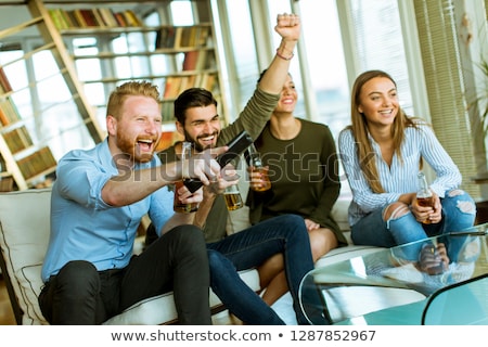 Foto stock: Group Of Young Friends Looking At The Tv Drinking Cider And Hav