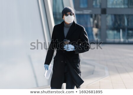 ストックフォト: Outdoor Shot Of Young Man In Black Coat Sterile Medical Mask And Protective Rubber Gloves Drinks T