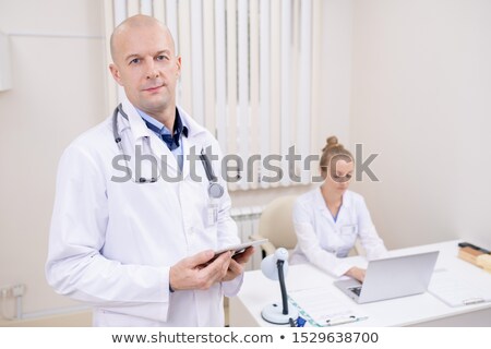 Foto stock: Bald Serious Professional In Whitecoat Looking Through Online Data In Clinics