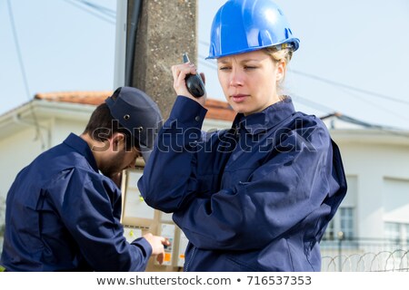 [[stock_photo]]: Female Electrician Taking Reading From Fuse Box